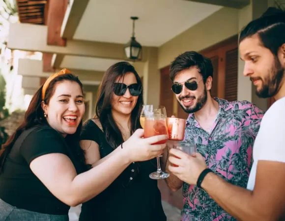 Quatre co-voyageurs souriants trinquant avec des cocktails en terrasse.
