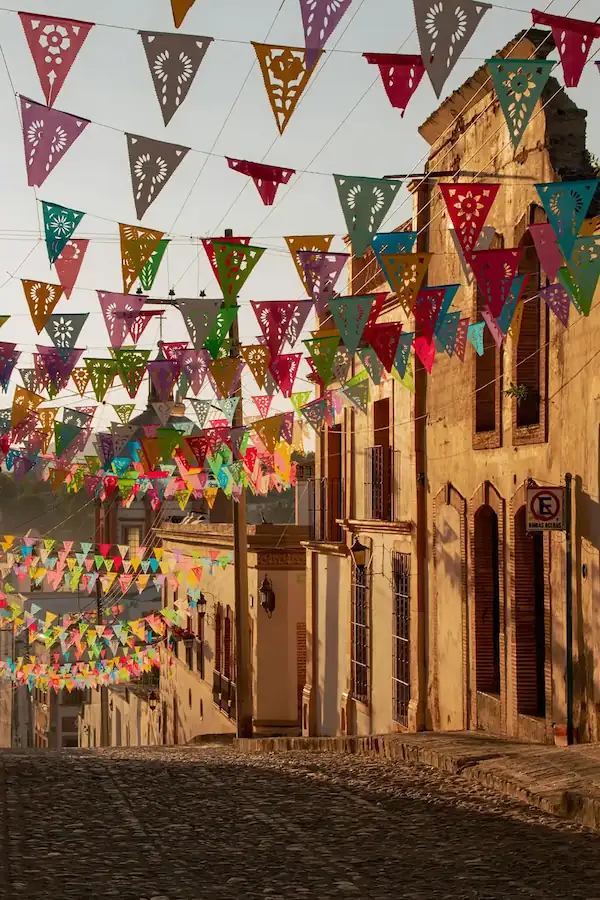 Ruelle pavée bordée de bâtiments coloniaux sous des fanions en papier découpé papel picado.