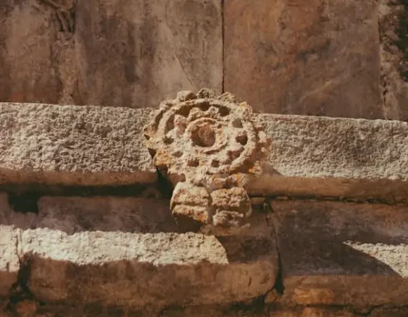 Gros plan sur un motif circulaire en pierre sculptée sur une frise murale à Uxmal.