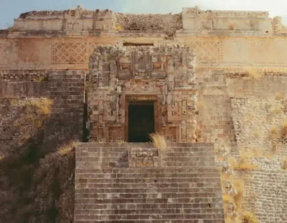 Escalier raide en pierre menant à une porte de temple ornée de frises et motifs géométriques mayas.