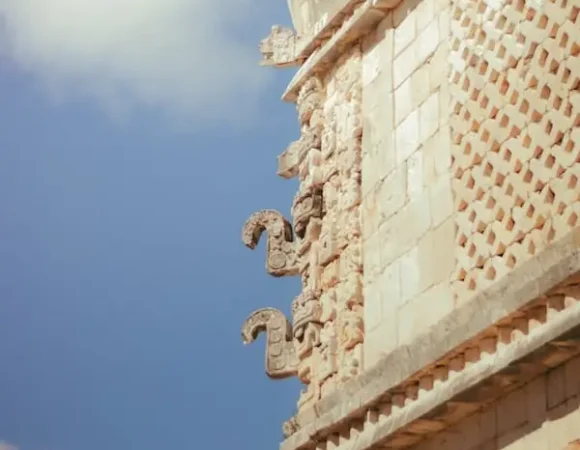 Angle d'un bâtiment en pierre montrant des masques empilés du dieu de la pluie Chaac avec leur nez crochu.