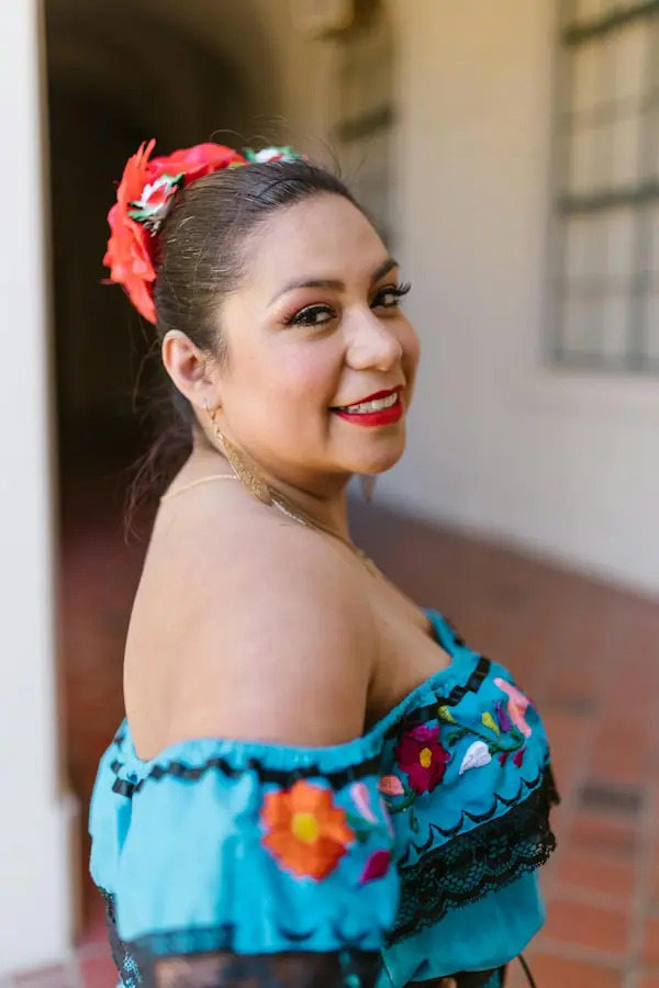 Femme mexicaine souriante portant une robe traditionnelle bleue brodée de fleurs et une fleur dans les cheveux.