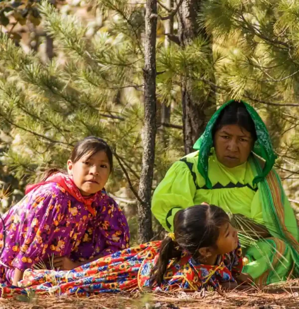 Femme et jeunes filles d'une communauté autochtone mexicaine habillées de robes traditionnelles vives assises en forêt.
