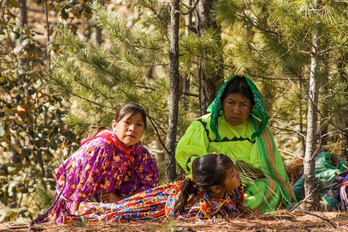 Femme et jeunes filles d'une communauté autochtone mexicaine habillées de robes traditionnelles vives assises en forêt.