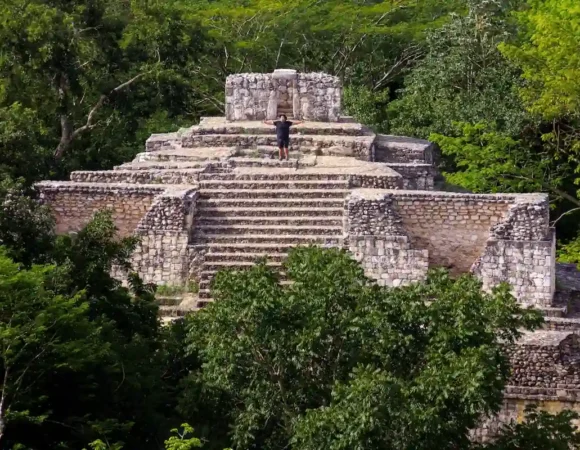 Personne debout les bras ouverts au sommet d'une pyramide maya en pierre entourée par une jungle verdoyante à Ek Balam.