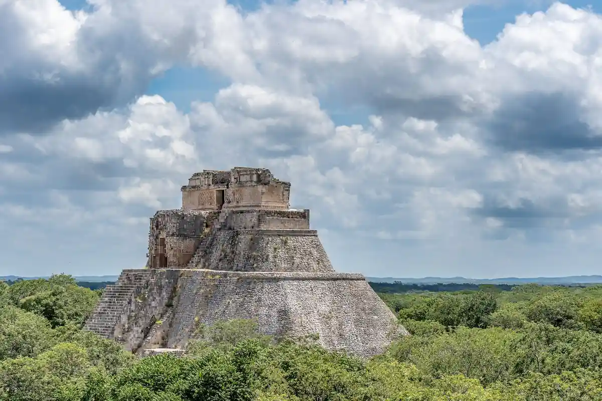 Vue panoramique de la Pyramide du Magicien à Uxmal s'élevant au-dessus de la canopée verte sous un ciel nuageux.