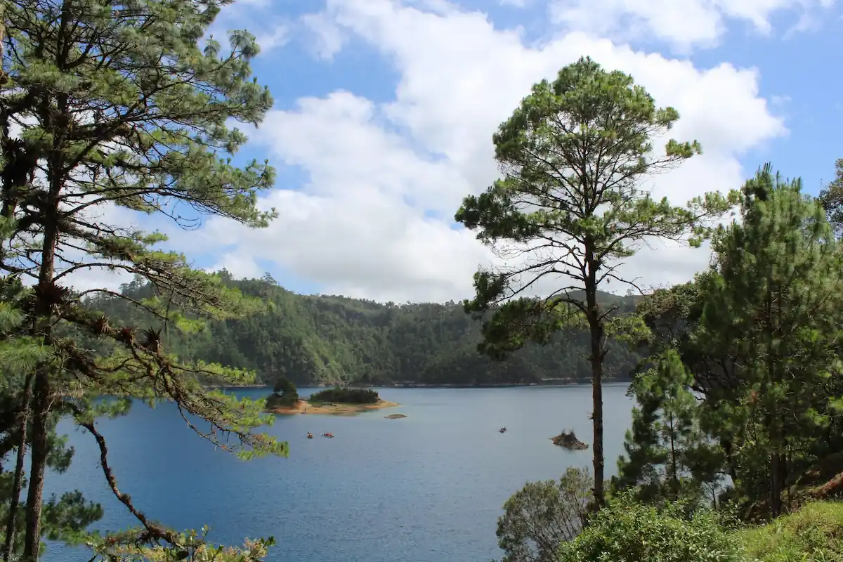 Vue panoramique sur un lac aux eaux bleu profond entouré de pins et de collines verdoyantes au Chiapas.