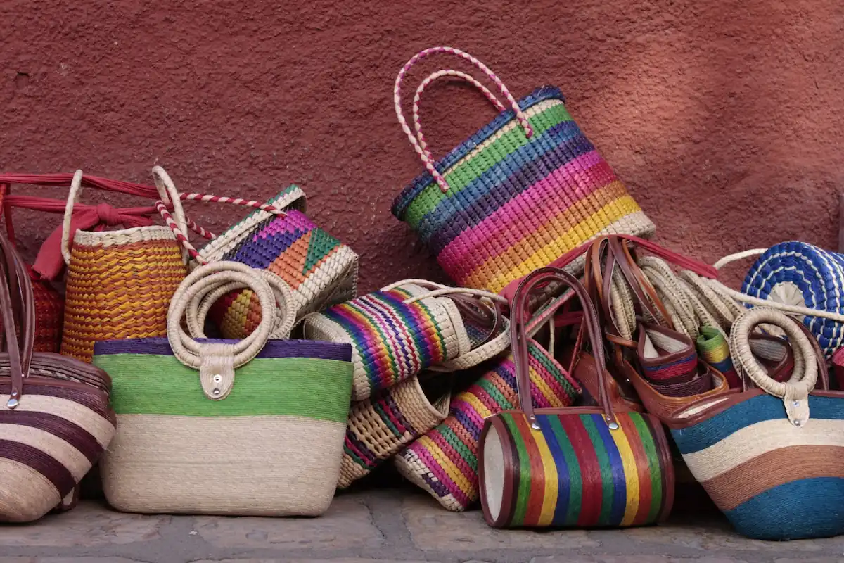 Collection de sacs colorés tissés à la main en fibres naturelles posés contre un mur en pierre.