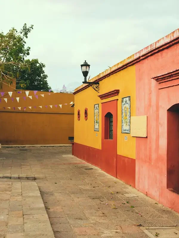 Rue pavée calme bordée de bâtiments coloniaux aux façades peintes en jaune et terre cuite sous un ciel clair.