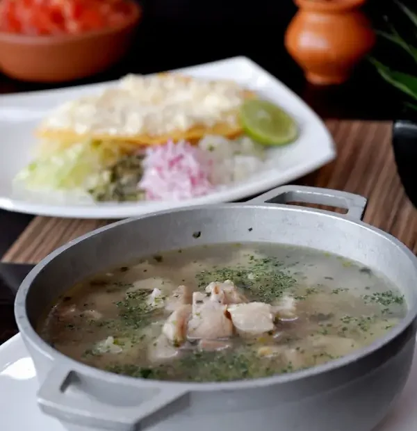 Bol en métal rempli de sopa de lima fumante garnie de volaille et d'herbes aromatiques.
