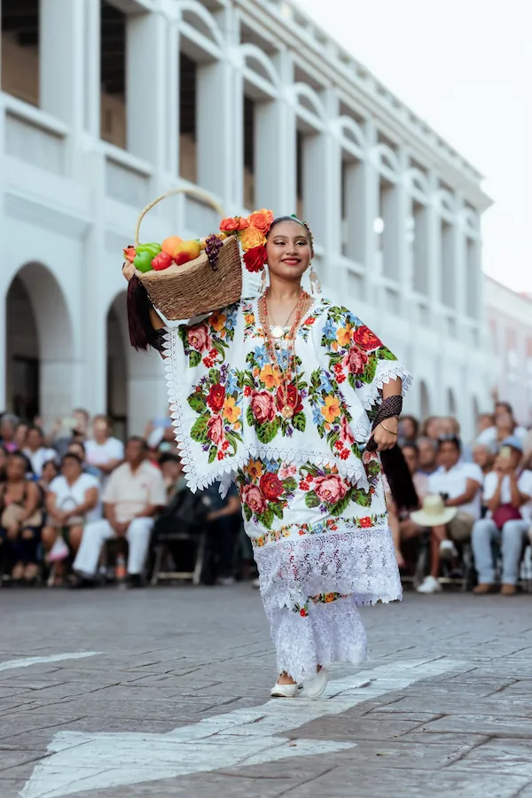 Jeune femme mexicaine vêtue d'un huipil traditionnel brodé de fleurs portant une corbeille de fruits.