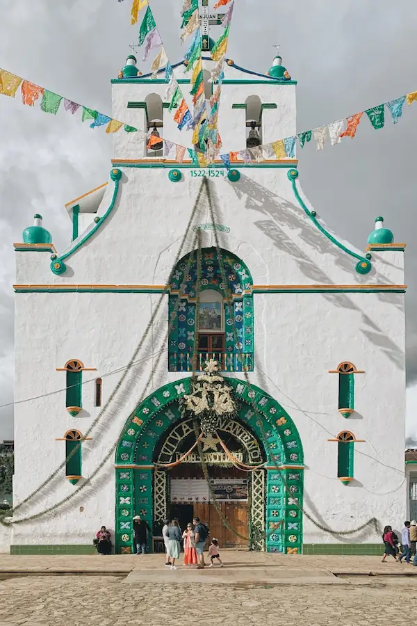Façade blanche et verte de l'église cérémonielle de San Juan Chamula ornée de fanions colorés.