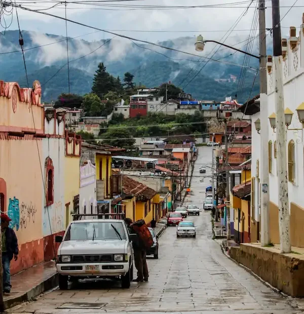 Rue pavée en pente bordée de maisons coloniales colorées avec des montagnes brumeuses en arrière-plan au Chiapas.